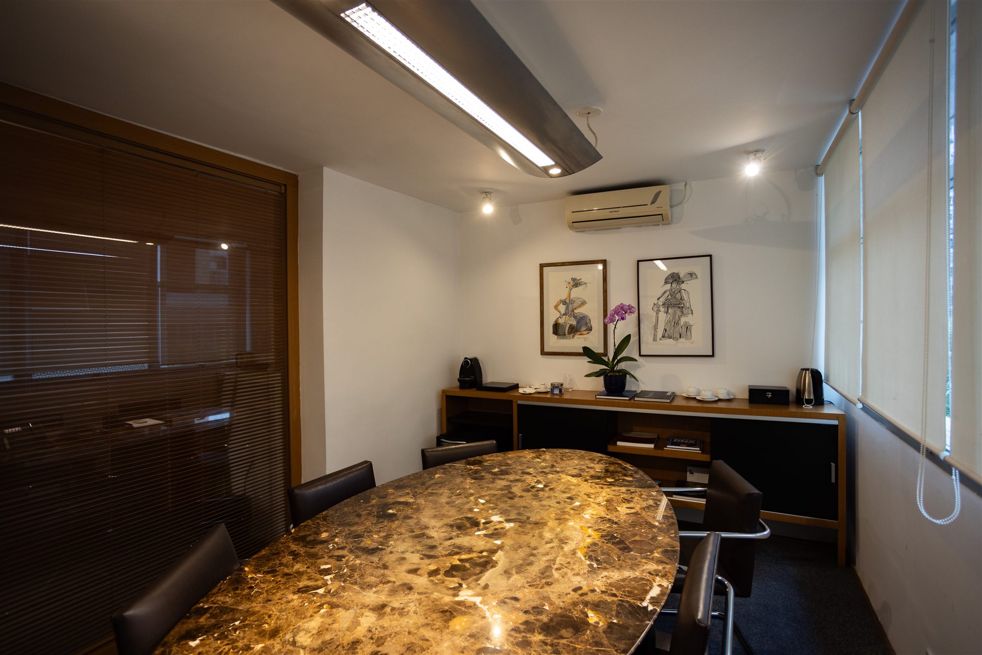 Sala de reuniões do escritório, com mesa oval em mármore, quadros e aparador